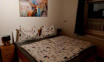 A cozy bedroom with a large bed and colorful cushions. On the wall hangs a colorful painting of a deer.