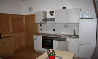 A modern kitchen with white cabinets and wood details. On the table sits a small plant in a red pot.