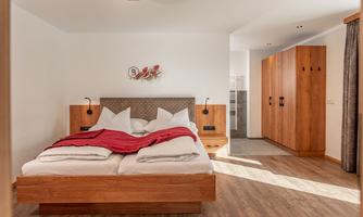A modern bedroom with a large double bed and a red throw. The room features wooden wardrobes and plenty of natural light.