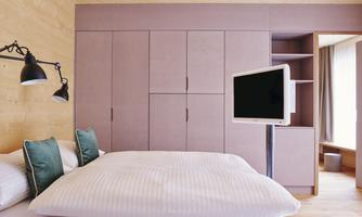 A modern bedroom with a large bed and elegant pillows. There is a television on the wall and a spacious wardrobe.