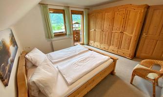 A bright bedroom with a wooden double bed and a large wardrobe. There are windows looking outside and a cozy atmosphere.
