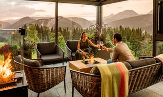 A cozy lounge area with a view of the mountains. A couple enjoys drinks at dusk.