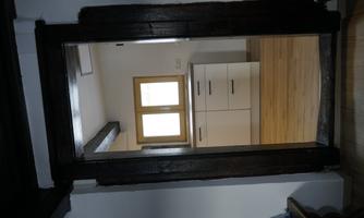 A view through a door into a modern kitchen with white furniture and a large window. The floor is made of light wood, which gives the room a friendly atmosphere.