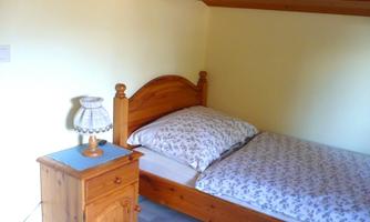 A simple bedroom with a single bed and a nightstand. Next to the bed is a small lamp.
