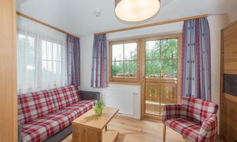A cozy living space with a checkered sofa and a wooden coffee table. Large windows offer a view of the nature outside.