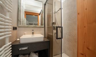 A modern bathroom with a shower, a sink, and a large mirror. Towels are neatly arranged in the under-sink cabinet.