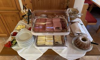 A rich buffet with cold cuts, cheese, and fresh sides. There are also some plates and a special cake.