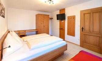 A modern bedroom with a large bed and bright wood interior. The room is well-lit and includes a desk as well as a television.