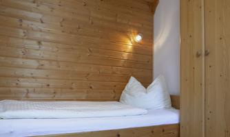 A cozy bedroom with wood paneling and a single bed. Next to the bed is a wardrobe that provides additional storage space.