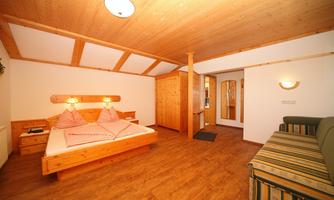 A cozy room with wooden paneling and a double bed. There is a seating area with a sofa and a large mirror.