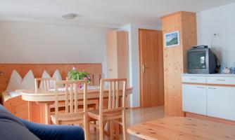 A bright and cozy living room with wooden details. There is a dining table, chairs, and a small seating area.