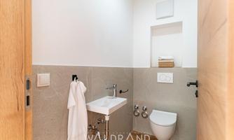 A modern bathroom with elegant furnishings. It features a sink, a toilet, and bright tiles.