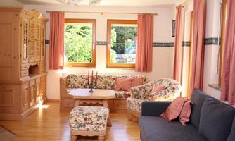A cozy living room with wooden furniture and comfortable upholstery. Daylight streams through the windows, creating an inviting atmosphere.