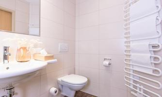 A modern bathroom with a toilet and a sink. The walls are in light colors and there is a towel warmer.