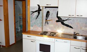 A modern kitchen with white cabinets and wooden accents. Intricate mosaics of birds can be seen on the wall.