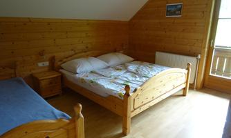 A simple bedroom with wooden decor. There are two beds, a nightstand, and a small balcony.