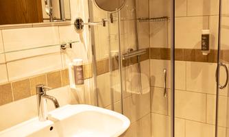 A modern bathroom with a shower cabin and sink. The walls are tiled and the furnishings are bright and inviting.