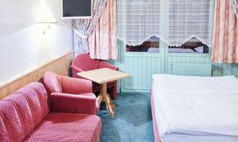 A cozy room with a red sofa and a table. The windows provide a view outside and are adorned with curtains.