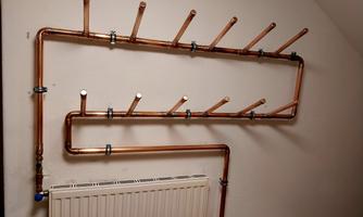 A wall installation made of copper pipes with several brackets. Below it is a radiator.