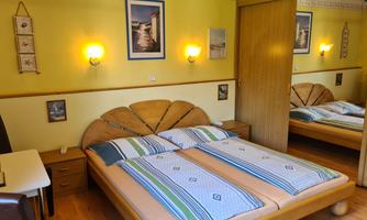 A cozy bedroom with a large double bed and yellow walls. The decor is simple, with a table and pictures on the wall.