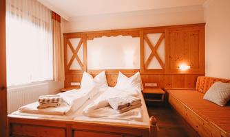 A cozy bedroom with wooden details and a large bed. Next to the bed is a couch, and the room has plenty of daylight.