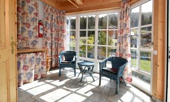 A bright conservatory with large windows and cozy furniture. The colorful curtains and wooden floor create an inviting atmosphere.