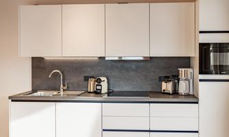 A modern kitchen with white cabinets and an elegant black work area. There is a sink, a coffee machine, and a kettle.