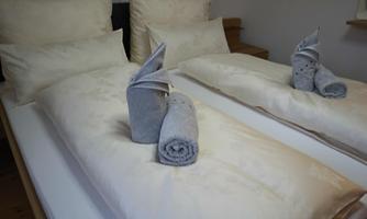 A tidy bed with white pillows and blankets. Towels are artistically folded into animal shapes.