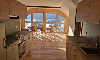 A modern kitchen with wood cabinets and large windows. The room is brightly lit and offers a view of the surroundings.