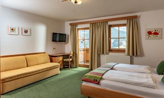 A cozy room with two beds and a sofa. Large windows offer a view of the surroundings and provide plenty of daylight.