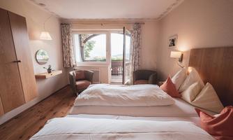 A cozy hotel room with two beds and modern furniture. Large windows offer a view outside and provide plenty of daylight.