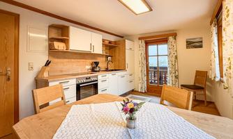 A modern kitchen with wooden cabinets and a dining area. On the table, there is a small vase with fresh flowers.