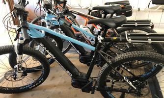 A series of electric bicycles is parked in a garage. The bicycles come in different colors and models.