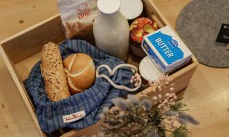 A wooden box with fresh rolls, milk, butter, and coffee. Some apples and dried flowers are also nicely arranged.