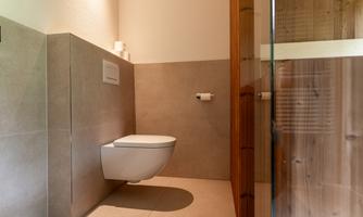 A modern bathroom with a simple toilet and a glass door. The walls are in neutral colors, creating a calm atmosphere.