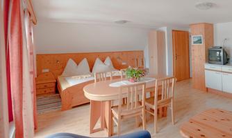 A cozy room with wooden decor, a dining area, and a sleeping area. Large windows let in plenty of light and create an inviting atmosphere.
