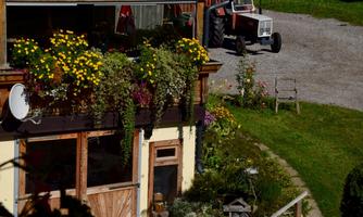 A farm building with colorful flowers on the balcony. In the background, a tractor is standing in a well-kept yard.