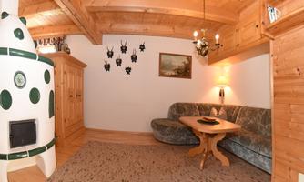 A cozy living room with wood paneling and a tiled stove. The furniture is inviting and traditional, ideal for relaxed hours.