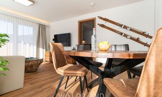 A modern living room with a stylish dining table and cozy chairs. Skis are hung on the wall, and large windows let in a lot of light.