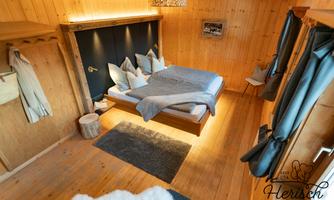 A cozy wooden bedroom with a double bed and modern pillows. The room is brightly lit and invites relaxation.