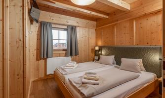 A cozy bedroom with wood paneling and two beds. The room features include a television and windows with curtains.
