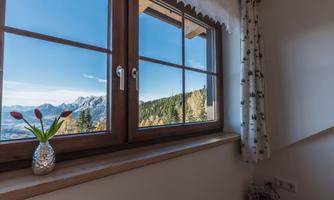 A window with a view of a beautiful mountain landscape and blue sky. On the windowsill, there is a small plant in a decorative vase.