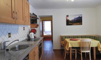 A cozy kitchen with wooden cabinets and a dining area. In the background, there is a room with a picture of mountains visible.