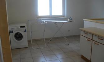 A bright laundry room with a washing machine and a clothes drying rack. There is a large window front that lets in a lot of light.