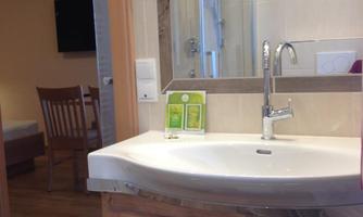 A modern bathroom with a sink and a large mirror. In the background, a chair and a shower are visible.