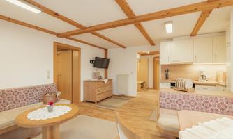 A bright and inviting living space with wooden beams and cozy seating. The kitchen is modern and well-equipped.