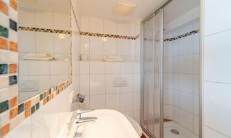 A bright bathroom with a shower and a sink. The walls are tiled and decorated with colorful accents.