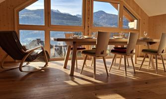 A cozy dining area with a table and chairs. Large windows offer a beautiful view of the mountains.