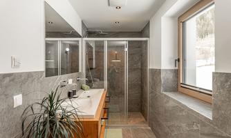 A modern bathroom with a glass shower and a wooden washbasin. Large windows provide plenty of natural light.