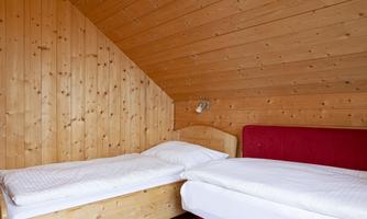 A cozy attic room with wooden paneling and two beds. A red sofa complements the simple but stylish decor.